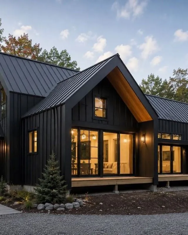 Dark modern home with a standing seam roof and lit windows